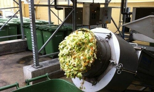 shredded food waste coming out of a grinder and into a green waste bin