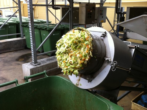 shredded food waste coming out of a grinder and into a green waste bin
