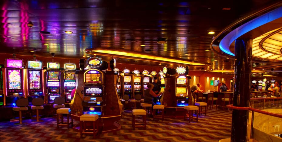 The inside of a dimly lit casino filled with slot machines. A few people are playing the slot machines.